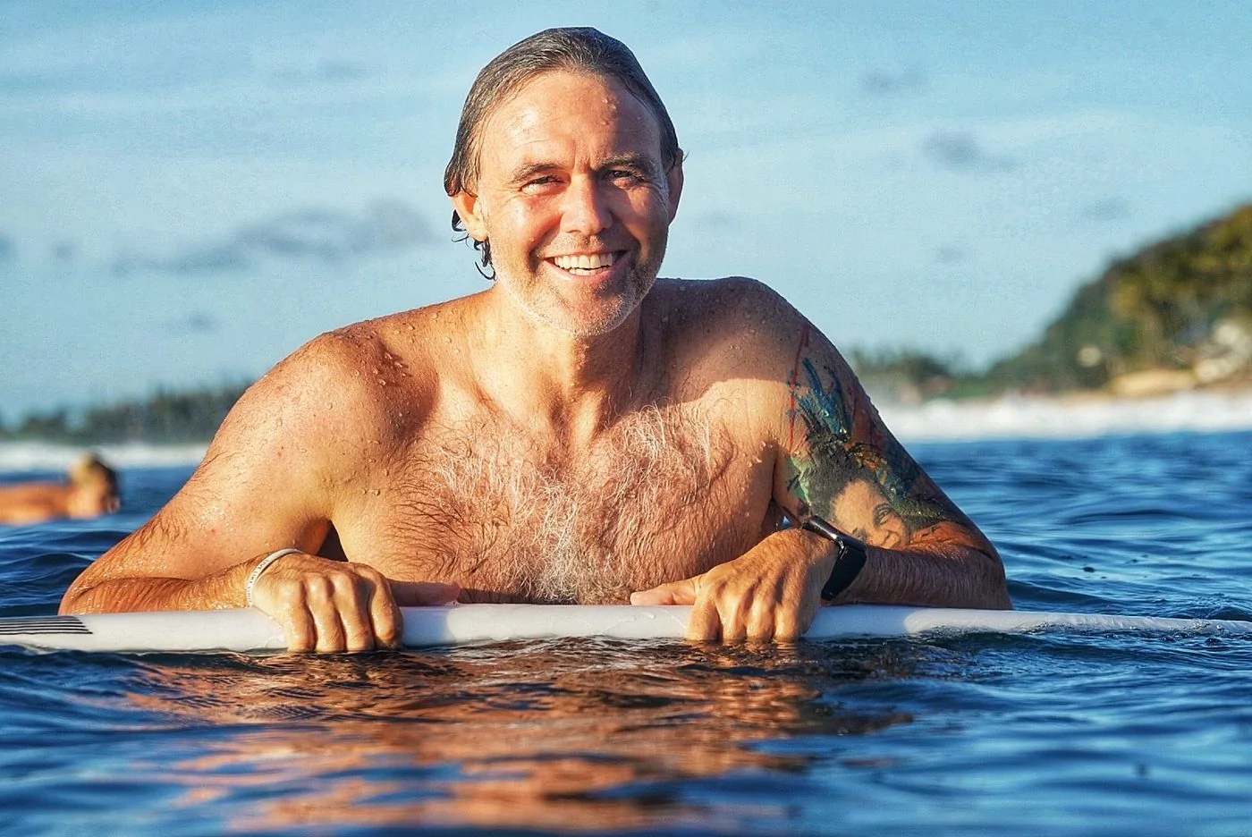 Chris Pierce in the water, resting on his board after a session